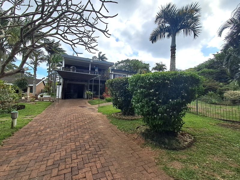 Front view of a two-story house featuring a brick paved driveway, established garden, and a covered upper-level balcony.