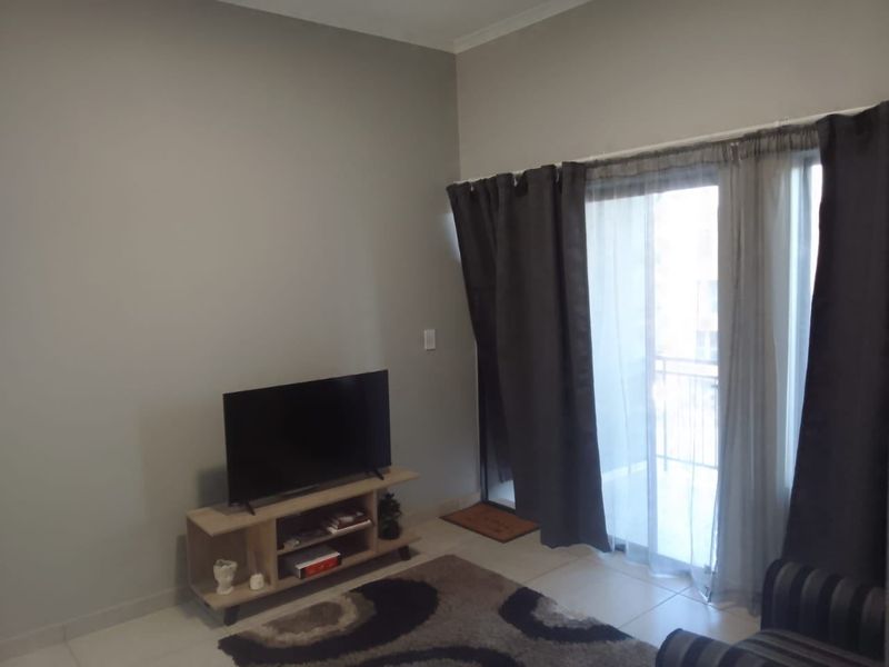 A living room area featuring neutral wall tones, tiled flooring, and a sliding glass door providing access to an outdoor balcony space.