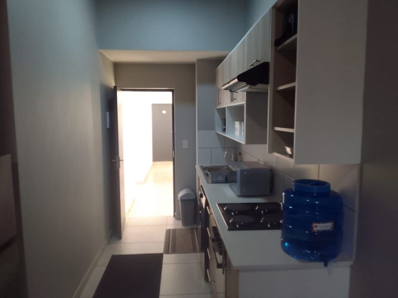 A compact kitchen featuring built-in cabinetry, an electric hob, an extractor fan, and a stainless steel sink, with tiled flooring throughout.
