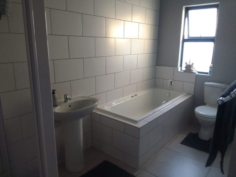 A clean, modern bathroom featuring a built-in bathtub, pedestal basin, and white subway-style wall tiling with natural light from a side window.