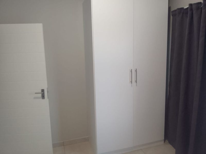 A clean, minimalist bedroom featuring a white built-in wardrobe and neutral tiled flooring, offering a blank canvas for personalization.
