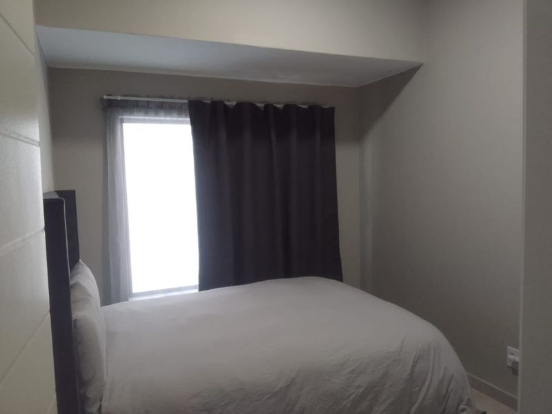A simple bedroom featuring a window with curtains and neutral wall finishes.