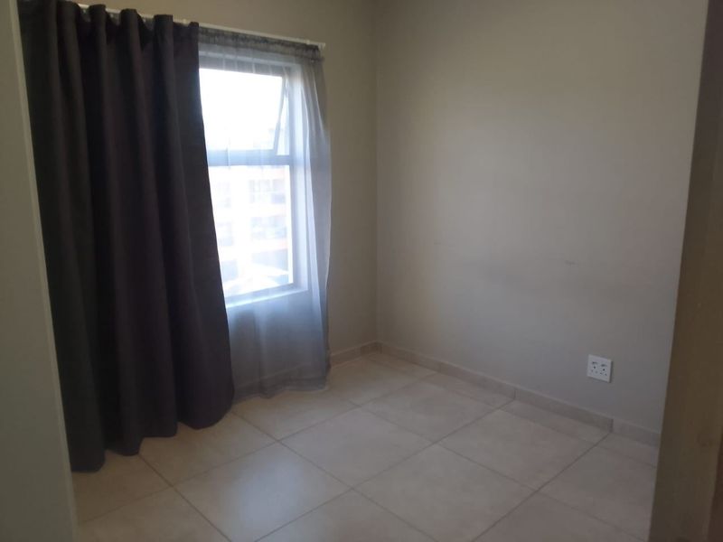 A clean, empty bedroom featuring neutral tiled flooring, a single window with curtains, and standard electrical wall sockets.