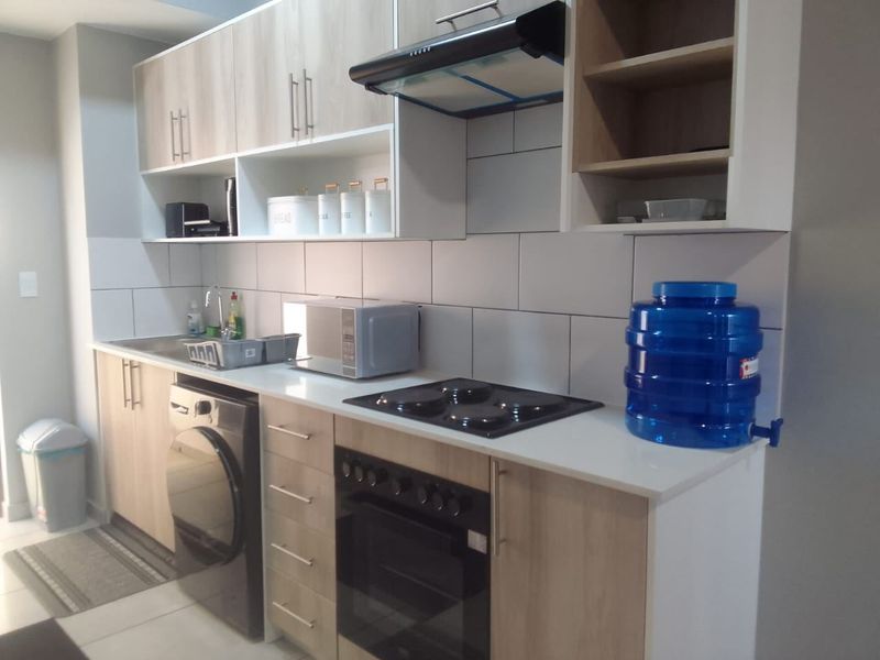 Modern kitchen featuring light wood-tone cabinetry, white tiled backsplash, integrated electric hob and oven, and durable tiled flooring.