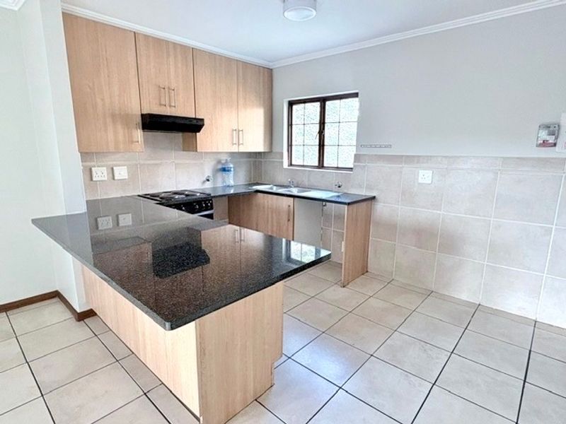 A functional kitchen featuring light wood cabinetry, dark granite countertops, a double sink, and tiled flooring with a neutral splashback.