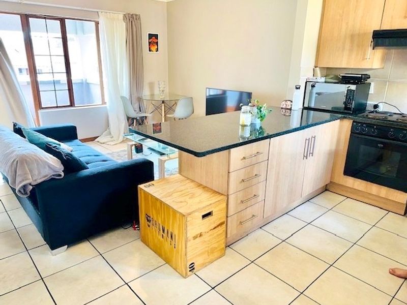 Open-plan living and kitchen area featuring tiled flooring, granite countertops, and built-in kitchen appliances, creating a functional and connected living space.