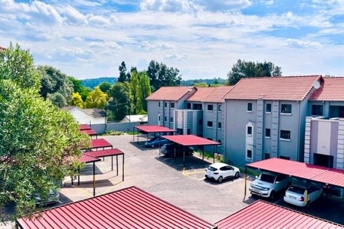 An elevated view of the apartment complex exterior, featuring multiple covered parking bays and paved driveway areas.