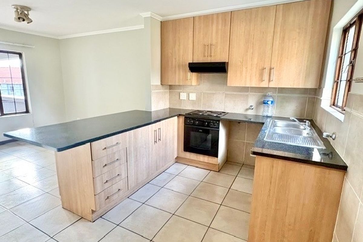 A clean, functional kitchen featuring light wood-finish cabinetry, dark granite countertops, built-in oven, gas hob, and tiled flooring throughout.