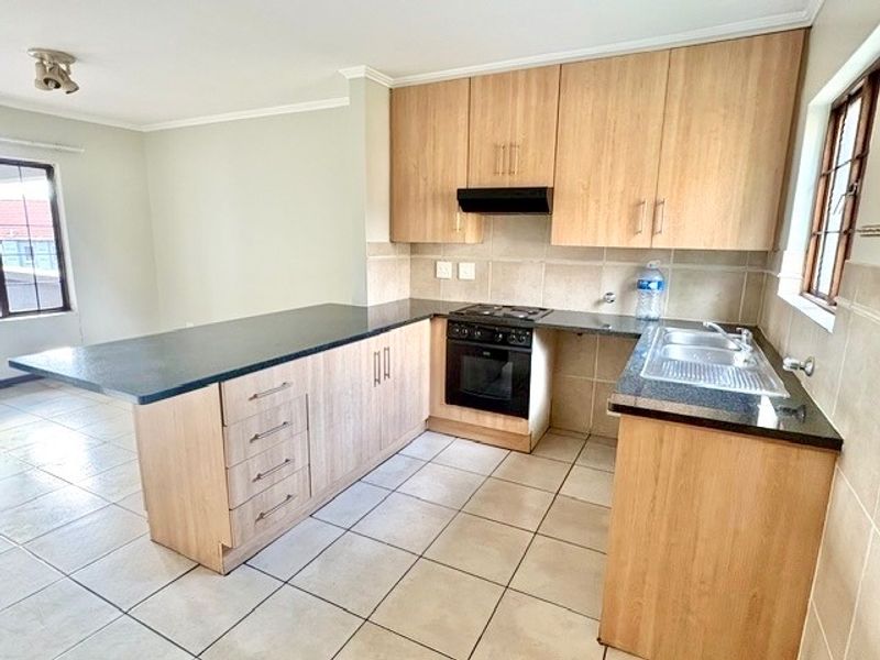 A clean, functional kitchen featuring light wood-finish cabinetry, dark granite countertops, built-in oven, gas hob, and tiled flooring throughout.
