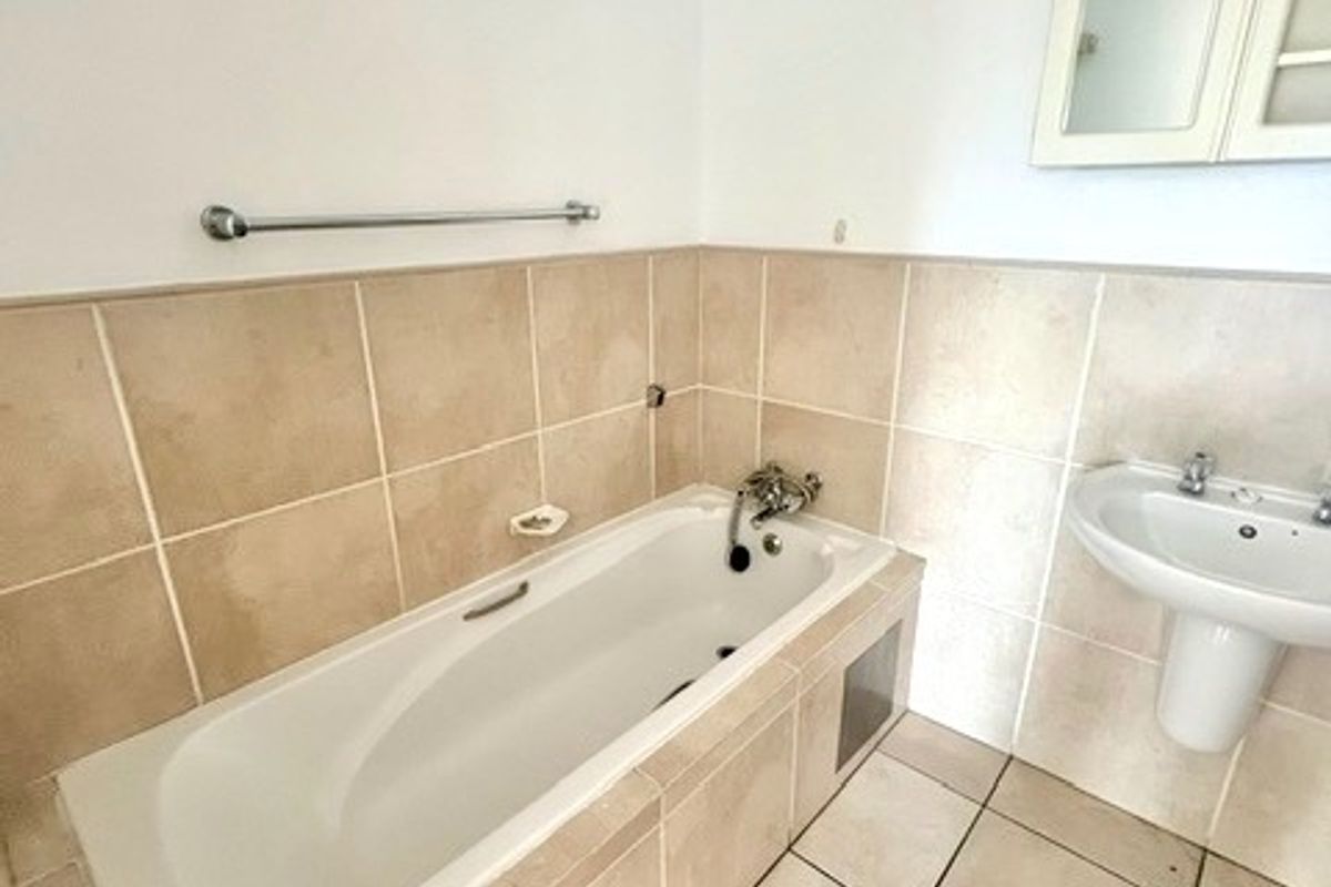 A clean, functional bathroom featuring a built-in bathtub, pedestal basin, and wall-mounted medicine cabinet with neutral ceramic tiling throughout.