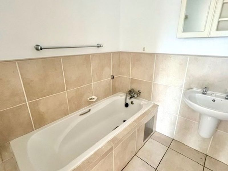 A clean, functional bathroom featuring a built-in bathtub, pedestal basin, and wall-mounted medicine cabinet with neutral ceramic tiling throughout.