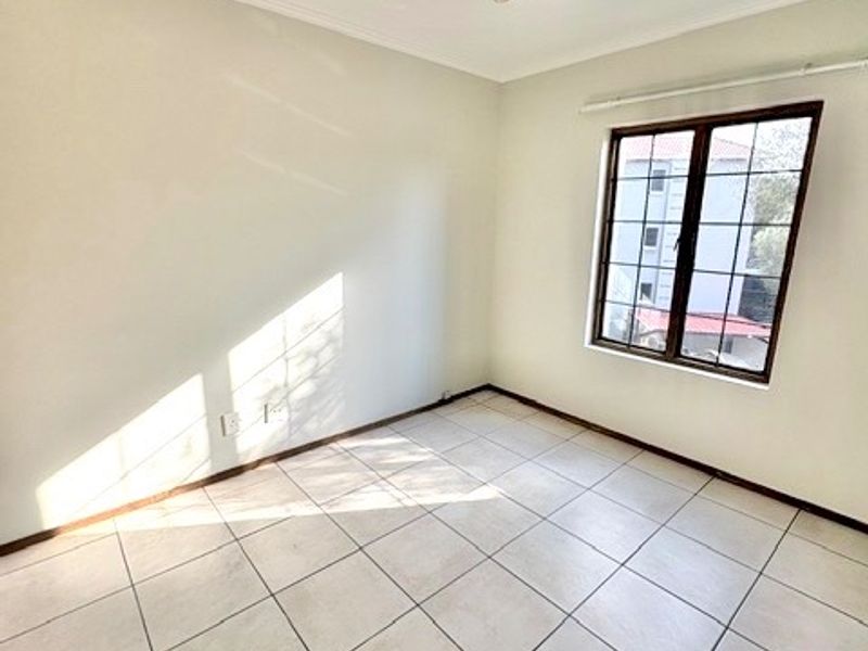 A bright, empty bedroom featuring neutral tiled flooring, a grid-pattern window, and a central ceiling light fixture.