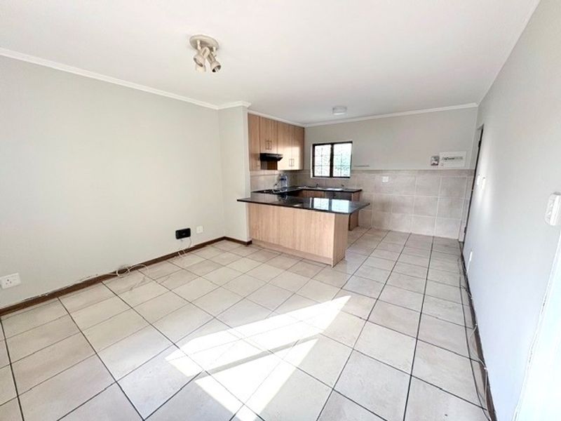 An open-plan living and kitchen area featuring tiled flooring, light wood cabinetry, granite countertops, and a breakfast bar in a clean, vacant space.