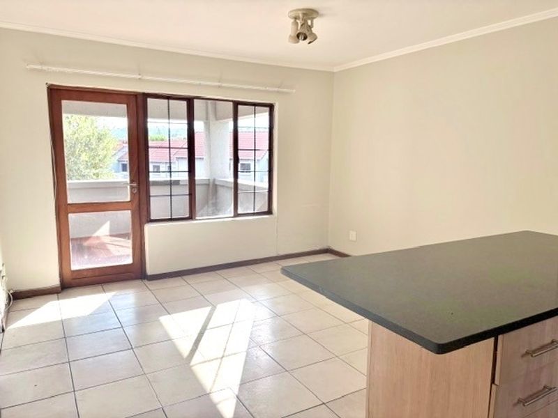 An open-plan living and kitchen area featuring tiled flooring, a kitchen island with built-in cabinetry, and direct access to a balcony through a glass door.