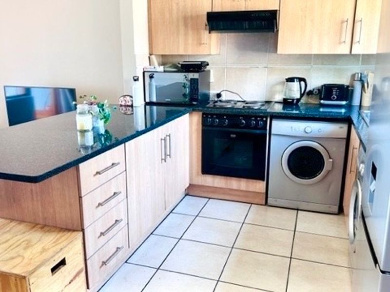 Compact kitchen featuring light wood cabinetry, granite countertops, built-in oven, hob, extractor fan, and integrated washing machine with tiled flooring.
