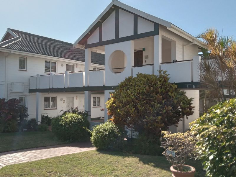 Exterior view of a multi-level apartment complex featuring a distinctive timber-frame style facade, upper-level balcony, and well-maintained surrounding garden area.