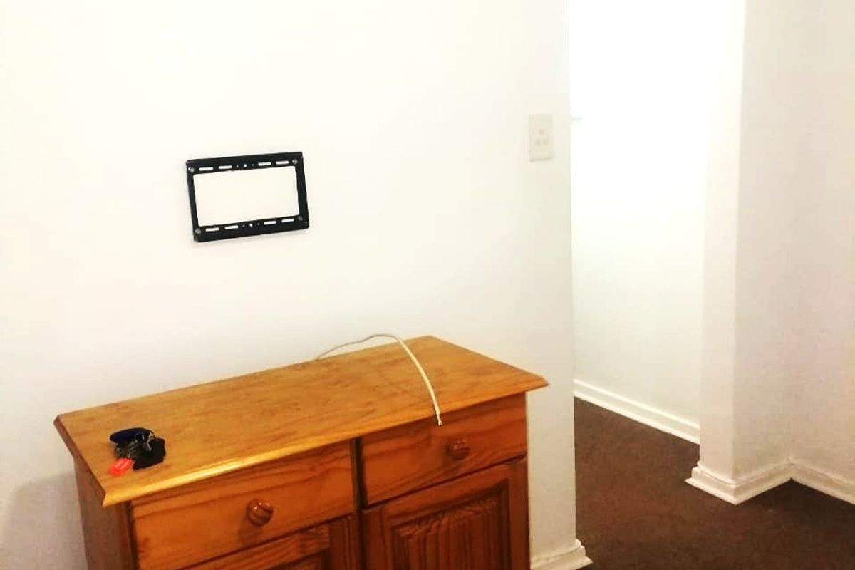 A simple living area featuring a wall-mounted TV bracket and neutral wall finishes, leading into an adjacent room.