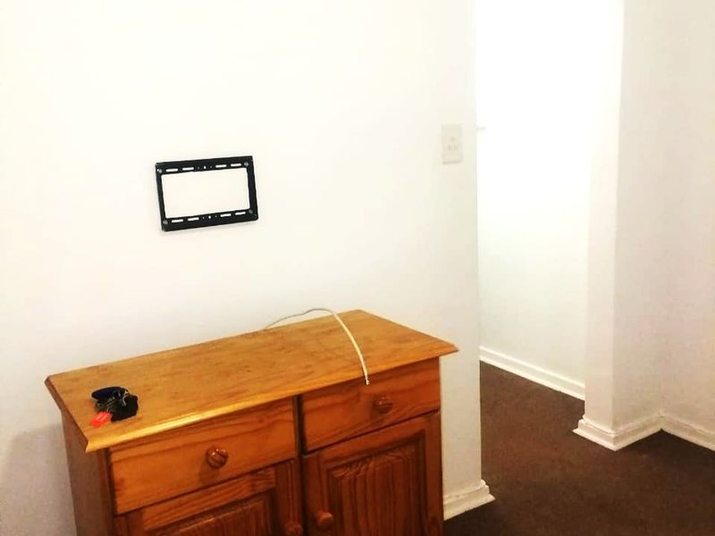 A simple living area featuring a wall-mounted TV bracket and neutral wall finishes, leading into an adjacent room.