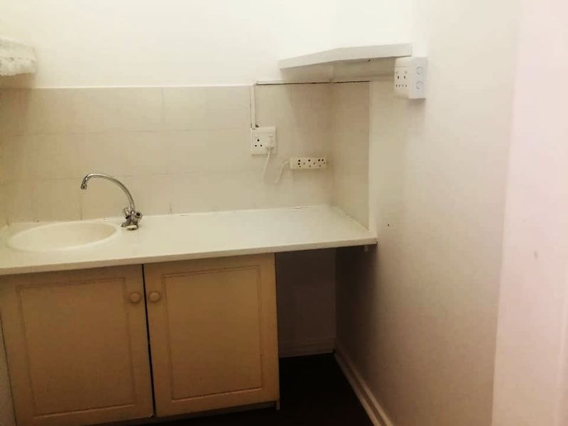 A compact laundry area featuring built-in cabinetry, a sink with faucet, and tiled splashback, providing a functional utility space.