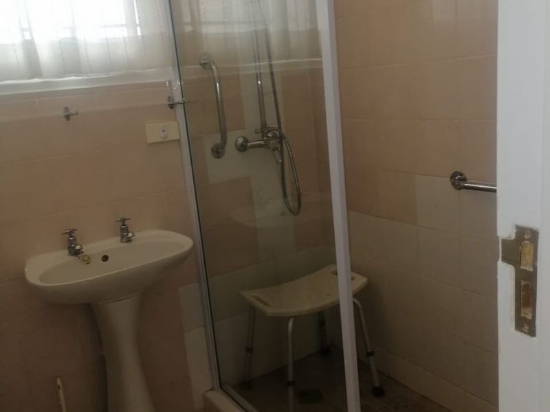 A functional bathroom featuring a pedestal basin, a glass-enclosed shower with a rainfall shower head, and installed safety grab rails.