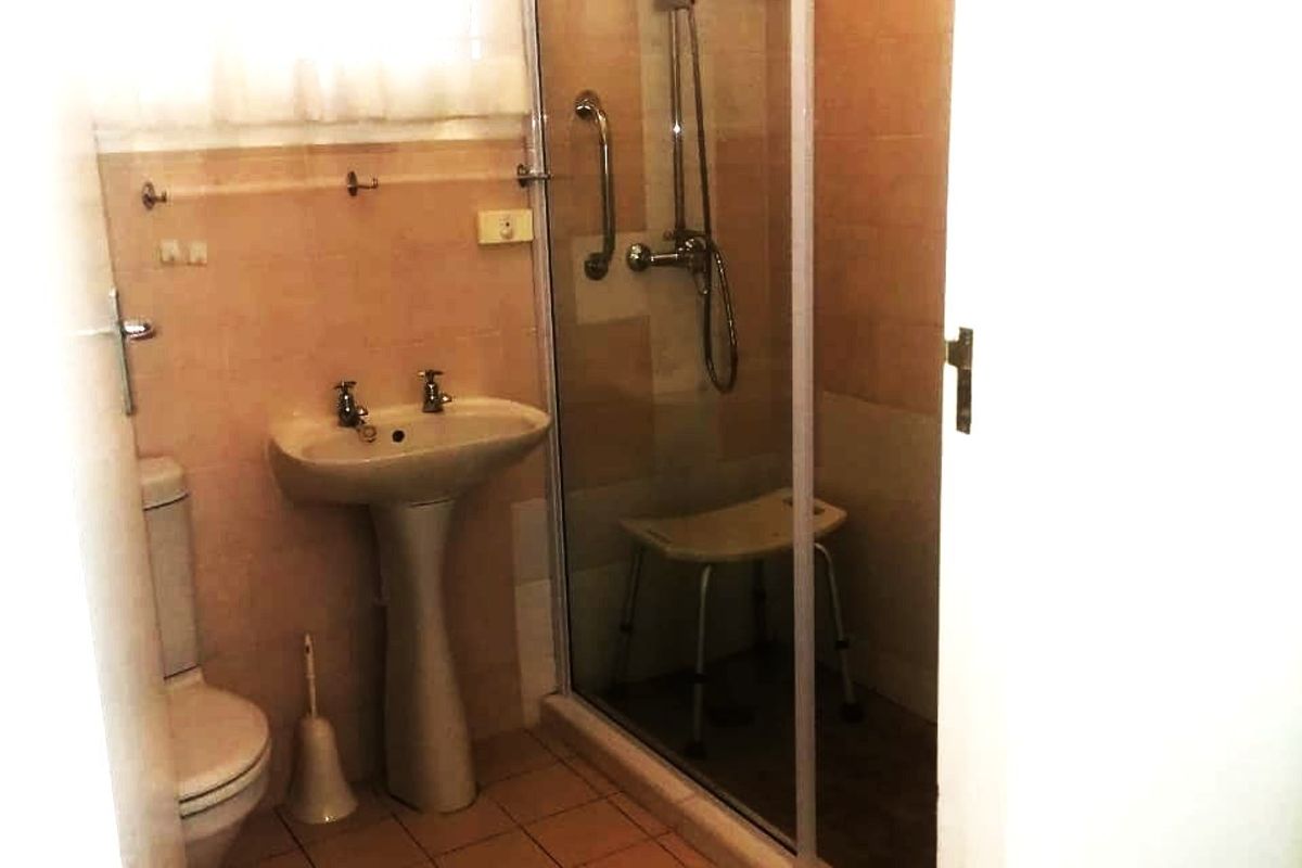 A functional bathroom featuring a pedestal sink, a glass-enclosed shower with a rainfall showerhead, and tiled finishes throughout.