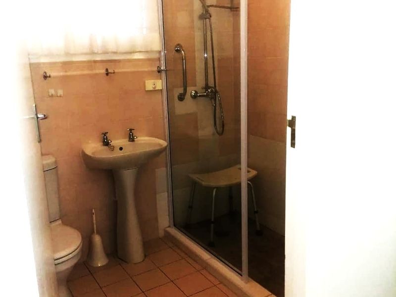 A functional bathroom featuring a pedestal sink, a glass-enclosed shower with a rainfall showerhead, and tiled finishes throughout.