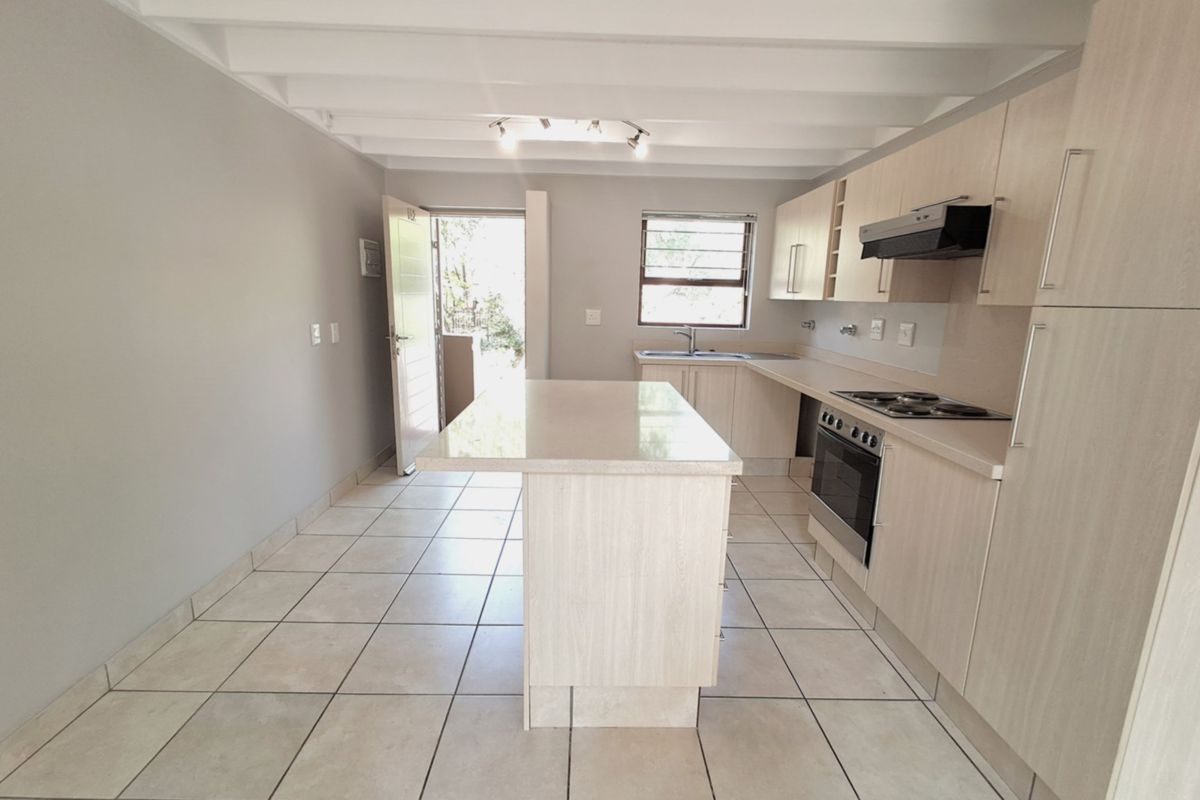 A bright, modern kitchen featuring light wood cabinetry, a central island, stone countertops, and tiled flooring, with direct access to an outdoor area.