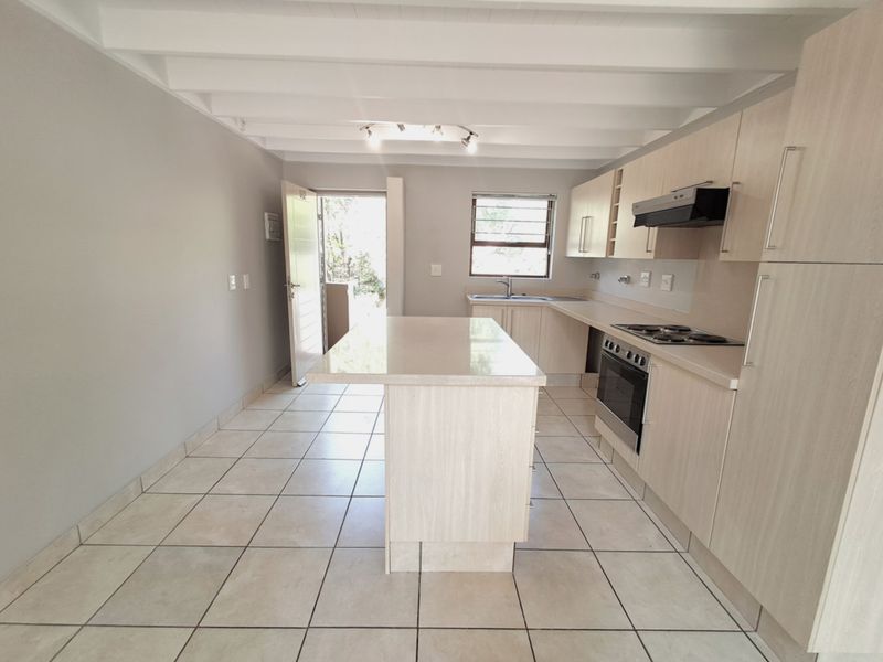 A bright, modern kitchen featuring light wood cabinetry, a central island, stone countertops, and tiled flooring, with direct access to an outdoor area.