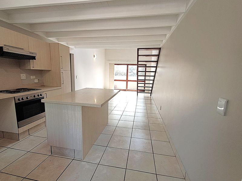 Spacious open-plan living area featuring a modern kitchen with island, tiled flooring, exposed beam ceilings, and a staircase leading to the upper level.