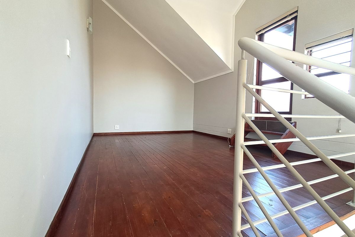 An empty loft-style bedroom featuring polished timber flooring, a sloped ceiling, and a modern metal balustrade overlooking the lower level.