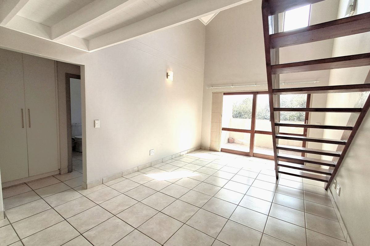 Spacious living area featuring vaulted ceilings with exposed beams, tiled flooring, a wooden staircase, and direct access to a balcony through sliding glass doors.