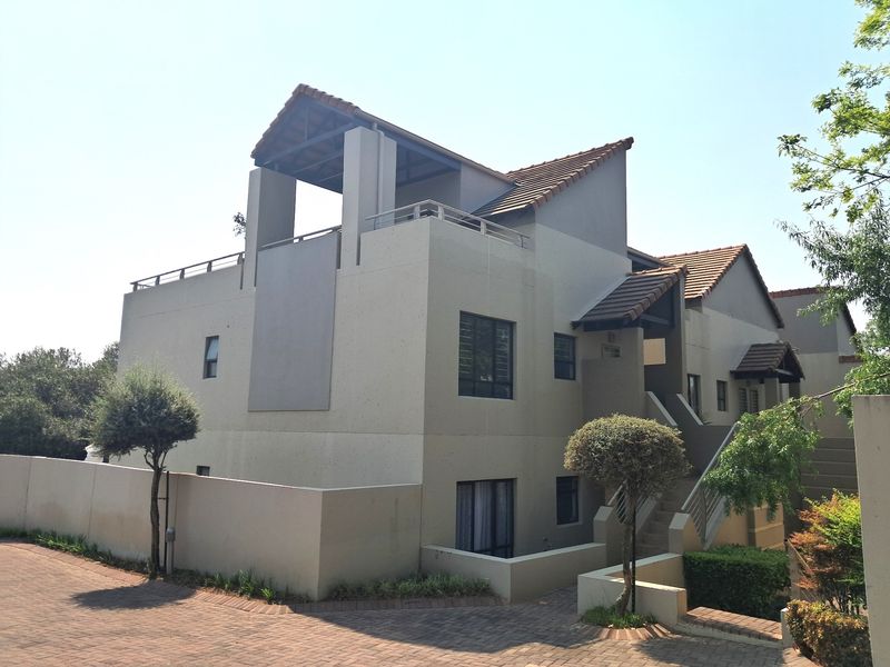 A multi-level apartment building exterior featuring a tiled roof, private balcony, and paved driveway access.
