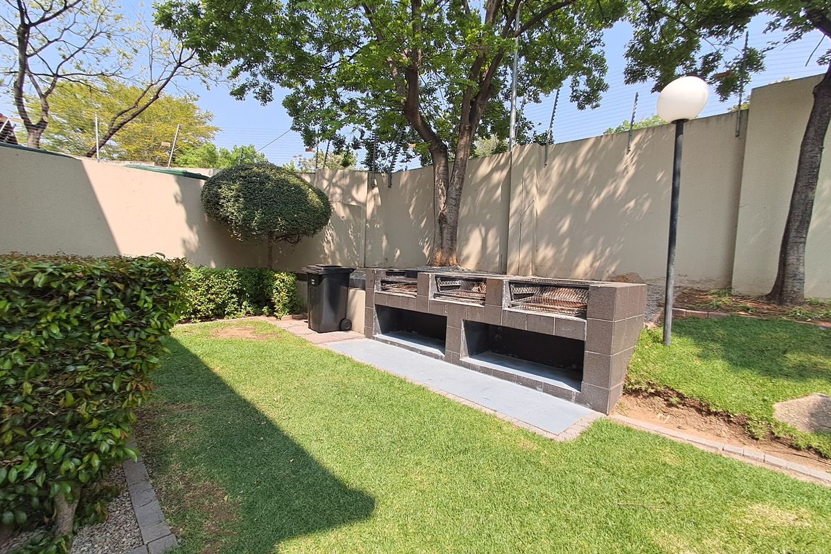A private rear garden area featuring a large built-in brick braai, manicured lawn, and secure perimeter wall with electric fencing.