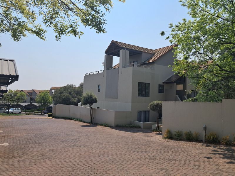 Exterior view of a multi-story apartment complex featuring a paved driveway, boundary walls, and a balcony with a tiled roof structure.