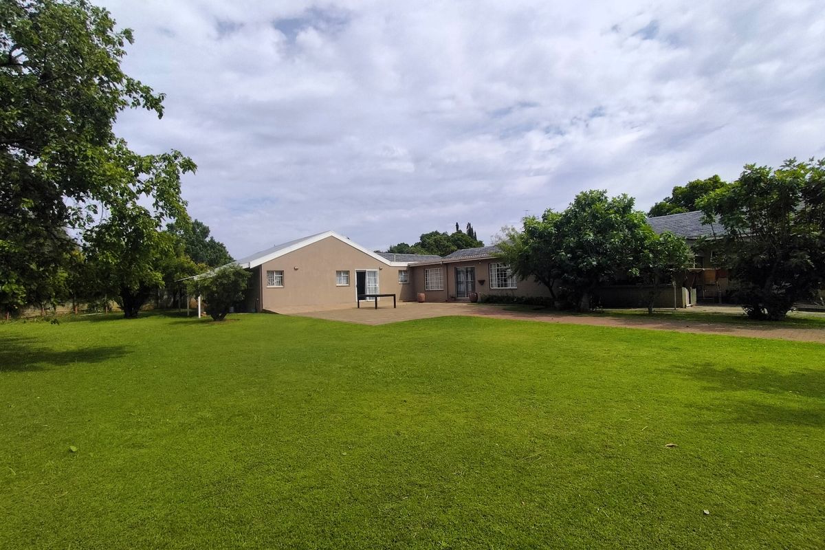 A spacious rear garden featuring a large lawn, mature trees, and a paved patio area adjacent to the house exterior.
