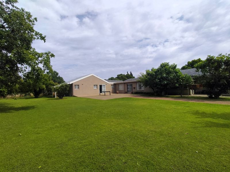 A spacious rear garden featuring a large lawn, mature trees, and a paved patio area adjacent to the house exterior.