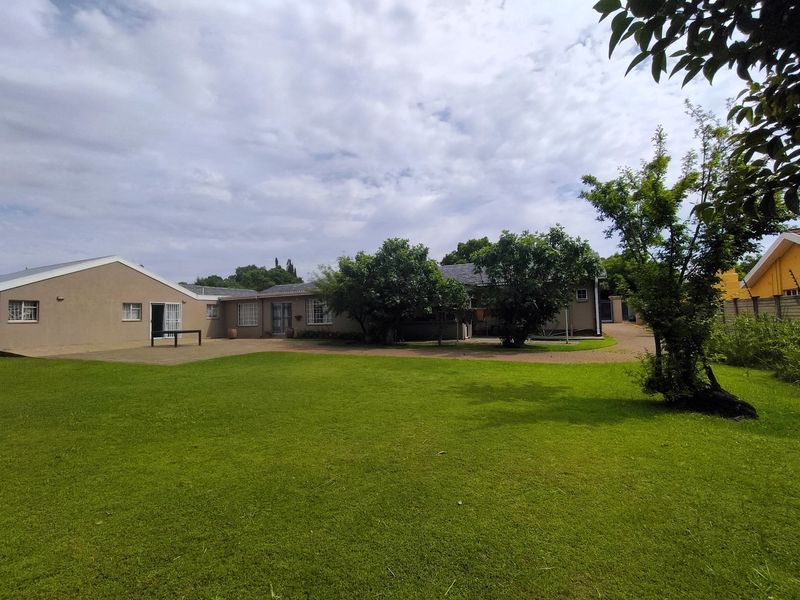 A spacious rear garden featuring a well-maintained lawn, paved patio area, and exterior access to the main house structure.