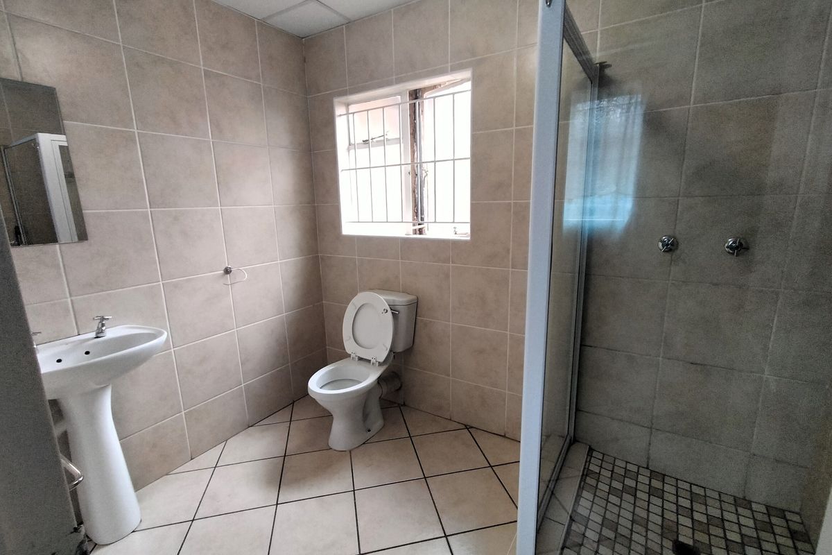 A functional bathroom featuring a pedestal basin, toilet, and a glass-enclosed shower with neutral wall and floor tiling.