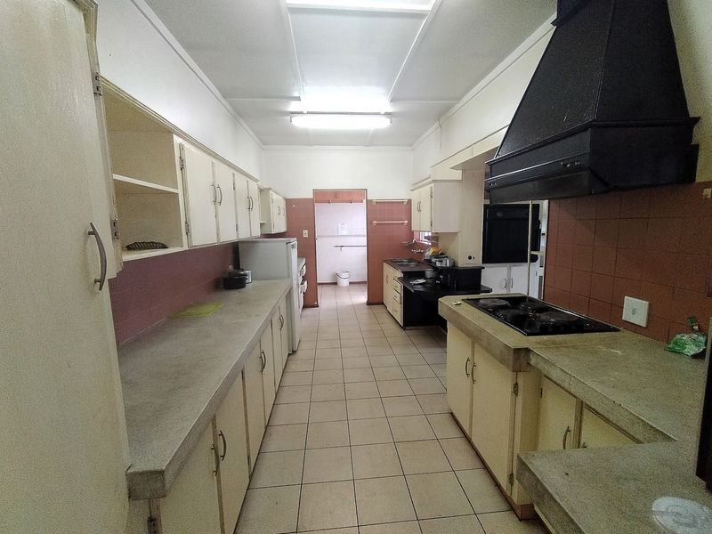 A dated galley-style kitchen featuring original cabinetry, concrete countertops, built-in hob, and extractor fan, offering significant potential for a modern renovation.