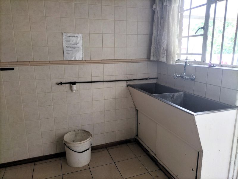 A functional laundry area featuring a double stainless steel sink, wall-mounted faucet, and tiled surfaces, providing a practical space for utility tasks.