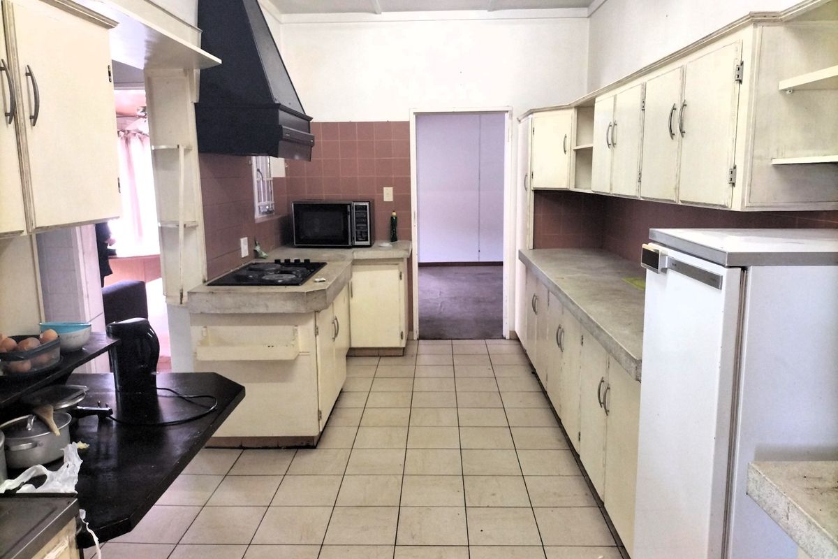 A dated kitchen featuring original cabinetry, concrete countertops, a gas hob with extractor fan, and tiled flooring, offering significant potential for modernization.