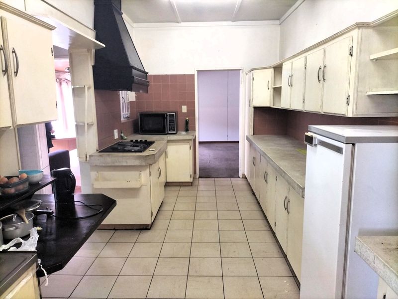 A dated kitchen featuring original cabinetry, concrete countertops, a gas hob with extractor fan, and tiled flooring, offering significant potential for modernization.