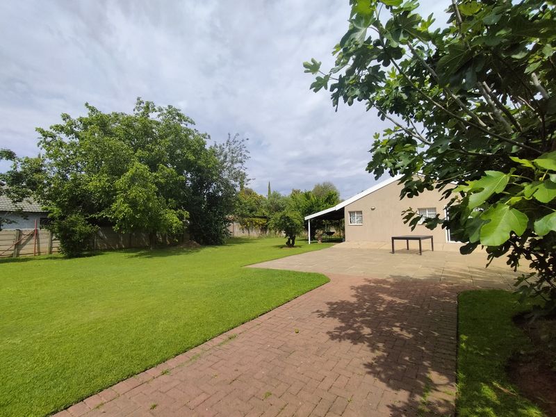A spacious rear garden featuring a paved patio area, brick pathway, and well-maintained lawn, providing a private outdoor space.