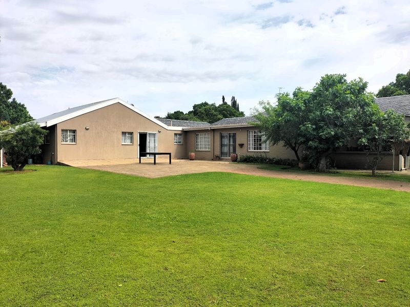 Spacious rear exterior view featuring a large paved patio area, well-maintained lawn, and established garden trees against the house facade.