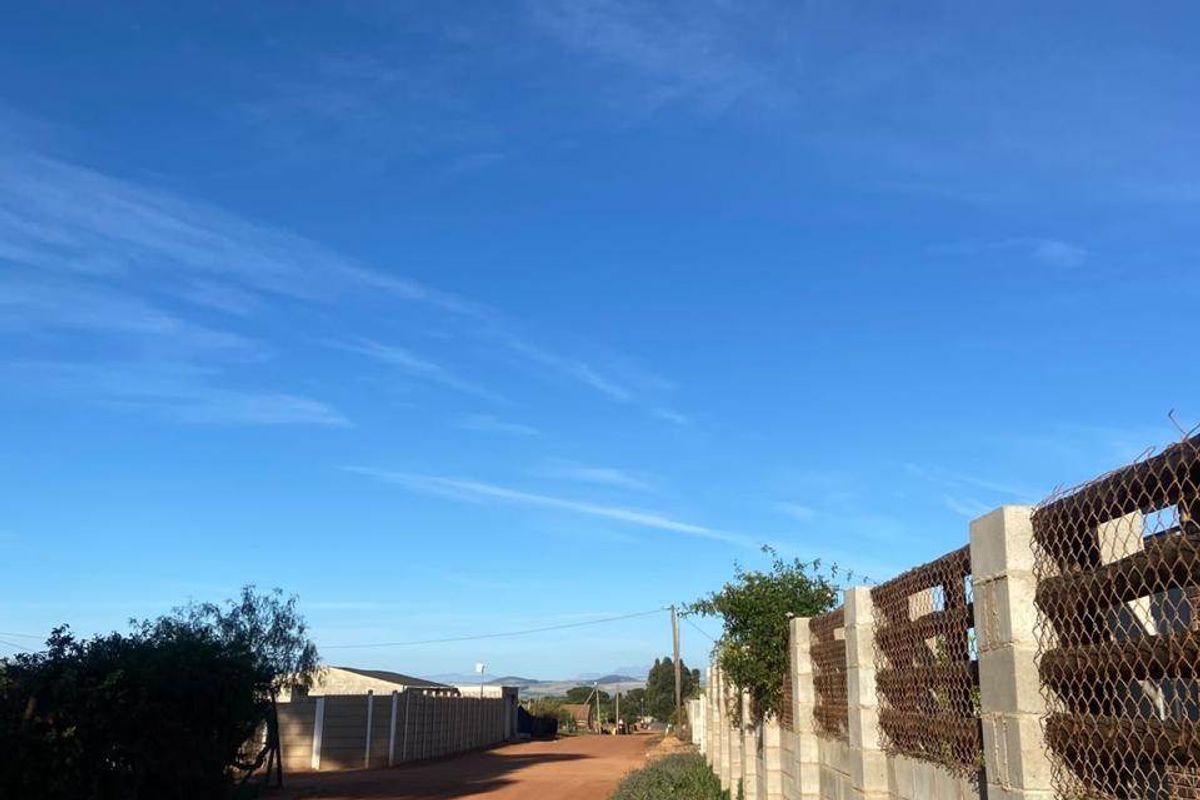 A view of an unpaved dirt road bordered by a concrete block boundary wall with wire mesh fencing.