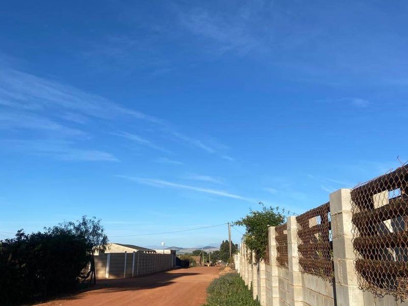 A view of an unpaved dirt road bordered by a concrete block boundary wall with wire mesh fencing.