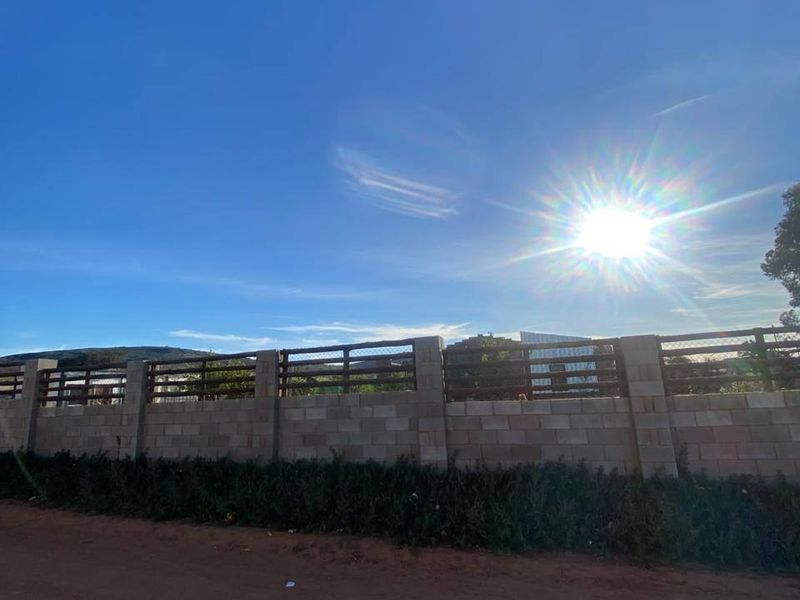 A view of the property boundary featuring a sturdy concrete block wall topped with timber slats, bordering a dirt road.