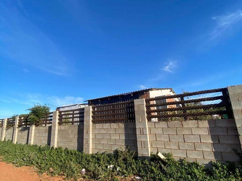A view of the property boundary featuring a concrete block wall with integrated metal mesh fencing along an unpaved road.
