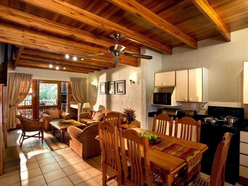 Open-plan living and dining area featuring a warm timber beam ceiling, tiled floors, and a functional kitchen with built-in cabinetry.