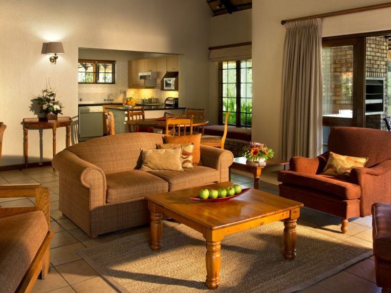 Spacious open-plan living area featuring tiled floors, vaulted ceilings with exposed beams, and a seamless flow to a kitchen and outdoor patio area.